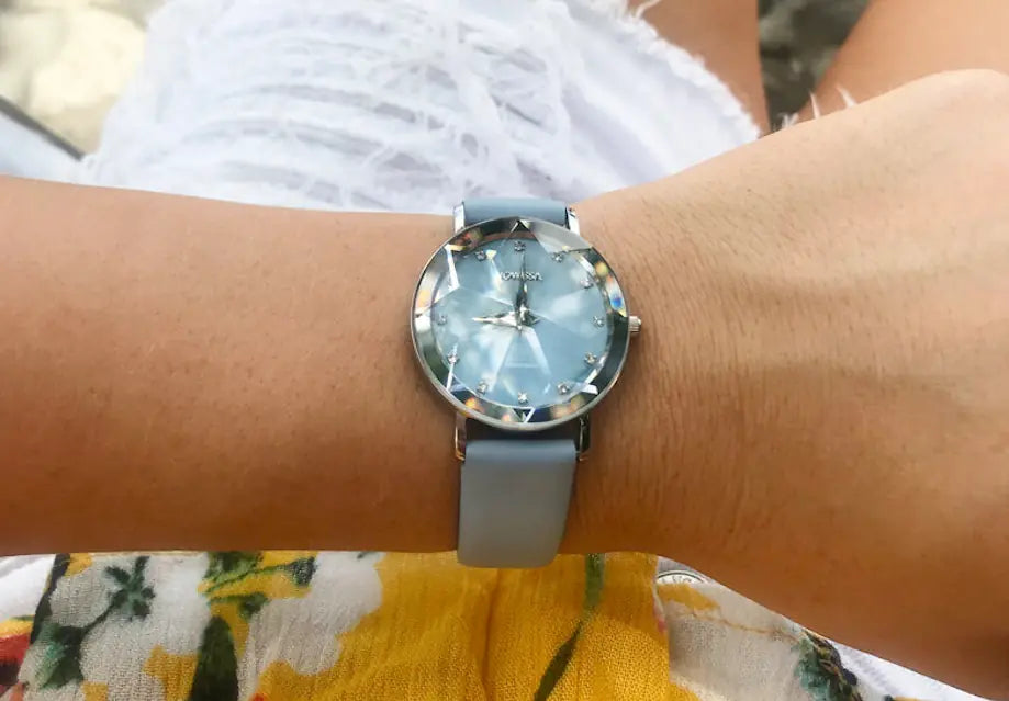 It' summer and a woman wears a beautifully facetted blue Jowissa watch on her wrist, seen from above while she is sitting on a chair.