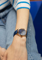 Beautiful watch worn by a girl - blue watch with gold elements - the watch has a calendar with date - the girl has a white shirt blue jeans - the watch is swiss made