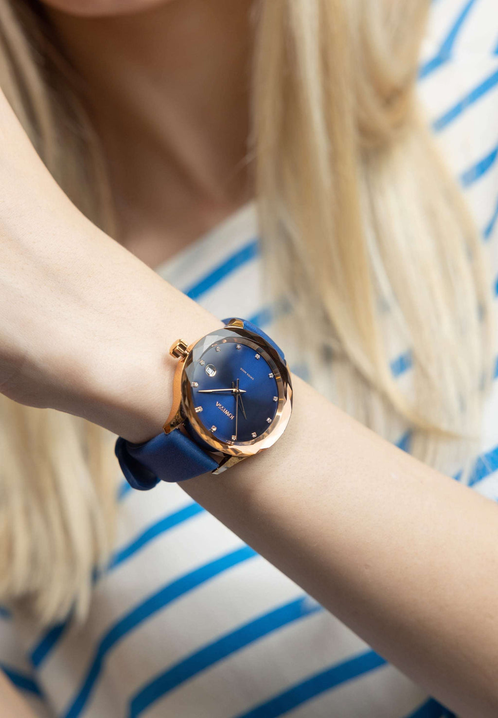 Blue watch - made for women - worn by a girl with a white shirt and blonde hair - the watch is blue with gold details - medium size watch