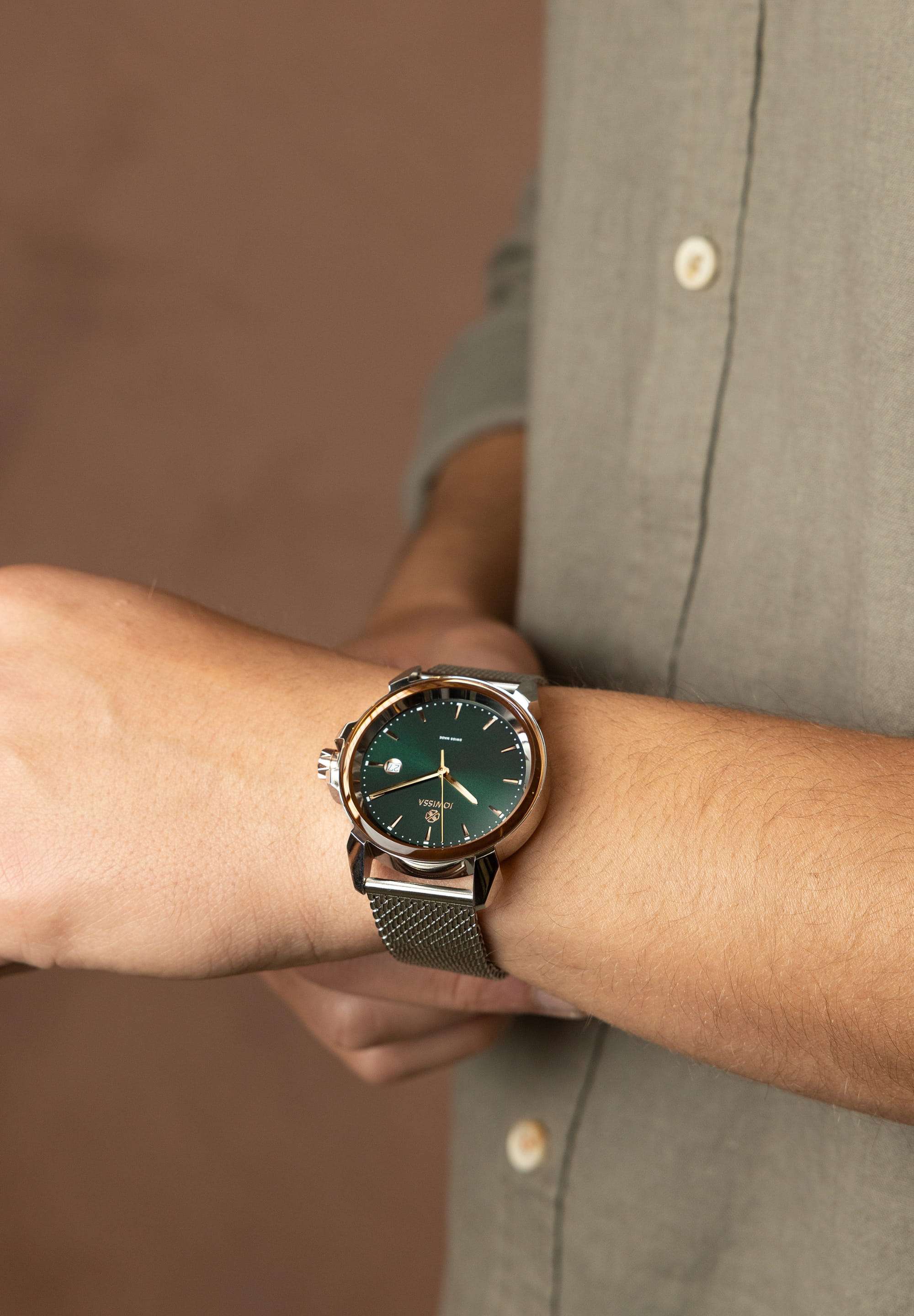 Swiss watch worn by a man who is wearing a grey shirt - the swiss watch has silver strap and green dial with gold details
