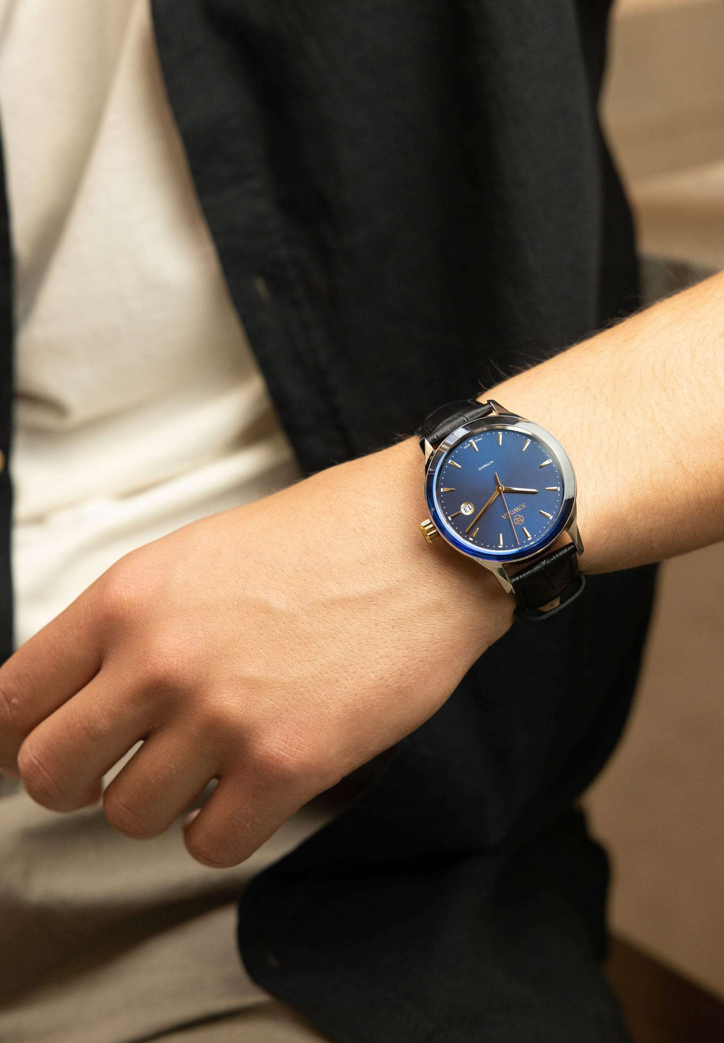 Blue mens watch with black leather strap - The watch is designed for comfort and durability, making it perfect for everyday wear or special occasions - worn by a men who is wearing white t-shirt blue shirt and grey pants 