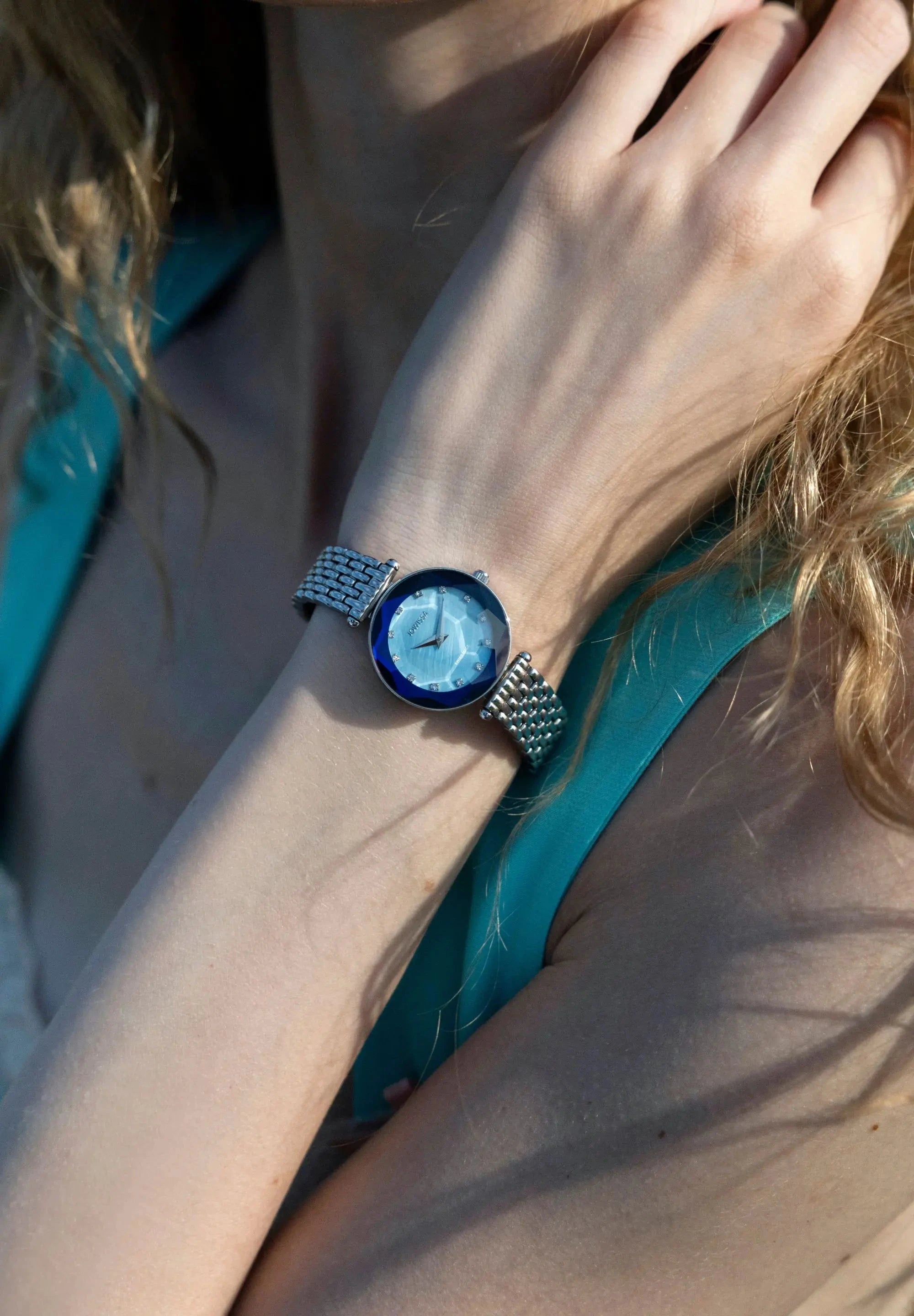 This silver Jowissa ladies' wristwatch presents a 27mm case with a captivating blue mother of pearl dial. Twelve rhinestones serve as hour indices, adding a touch of brilliance. The faceted mineral crystal and the stainless steel bracelet in silver look stunning. All Swiss Made.