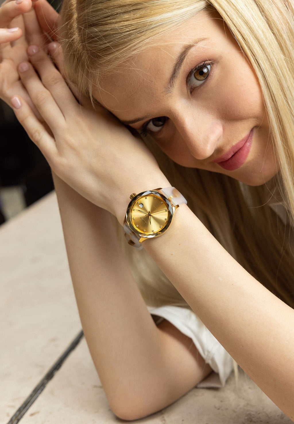 J6.243.M medium size watch– worn by a blonde girl - women’s watch features a gold-plated stainless steel case paired with a sleek black sunray dial adorned with 12 rhinestone hour markers - includes a calendar window. All swiss made