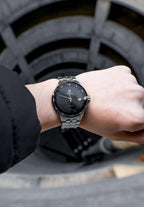 Romo Swiss watch made for men. Worn by a man showing his hand. Has a stainless steel case with a gloss polished surface and shiny, sunray dial. Equipped with a Ronda 515 Swiss quartz movement, it features a date window and Dauphine-style hands. The watch is water-resistant up to 5 ATM and protected by tempered mineral glass. Made in Swiss