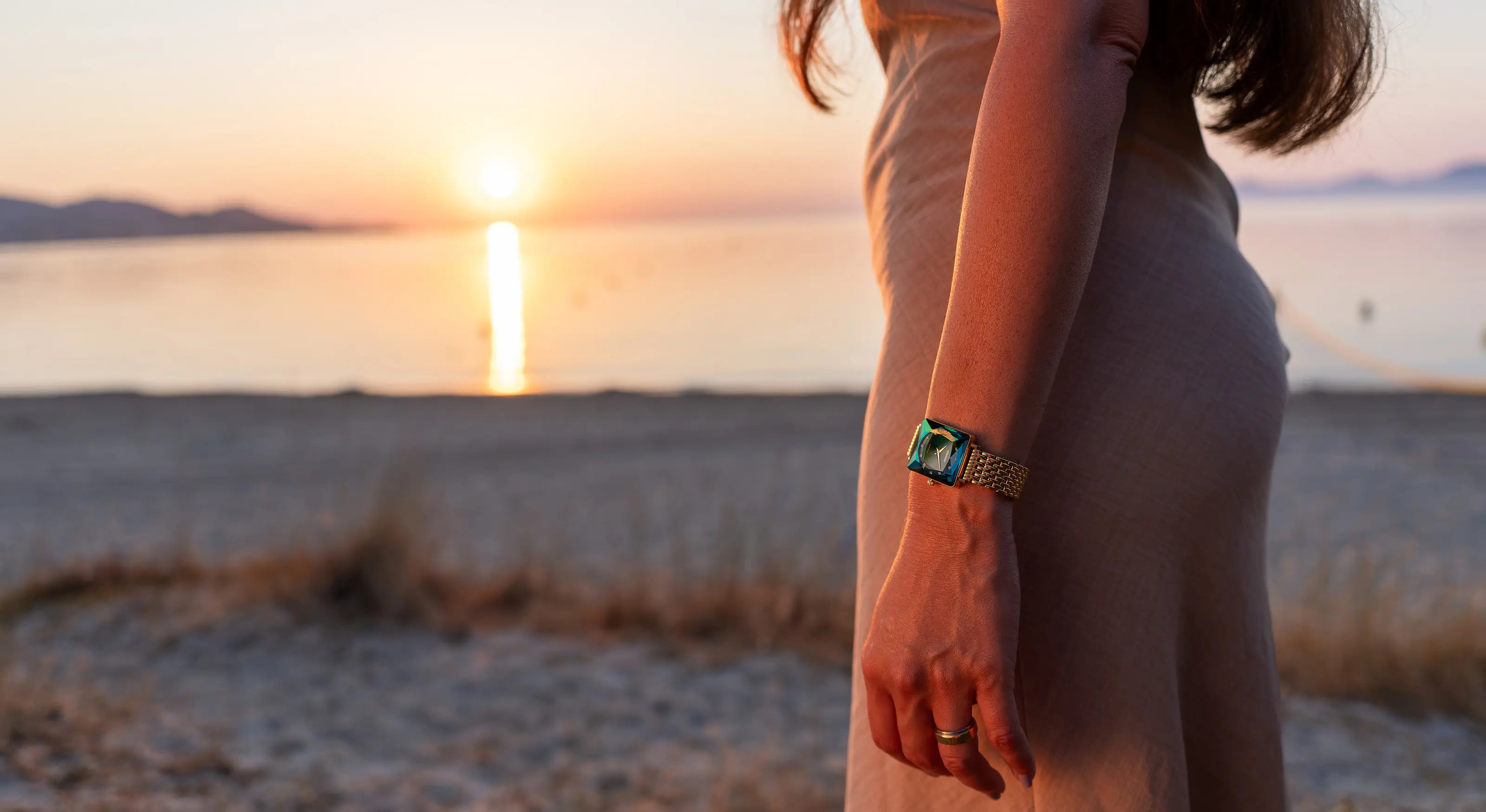 Woman at sunset wearing the elegant Jowissa Facet Princess Swiss Made square women's watch, showcasing a green dial, diamond-cut glass, and gold bracelet. Affordable Swiss Luxury Watches by Jowissa.