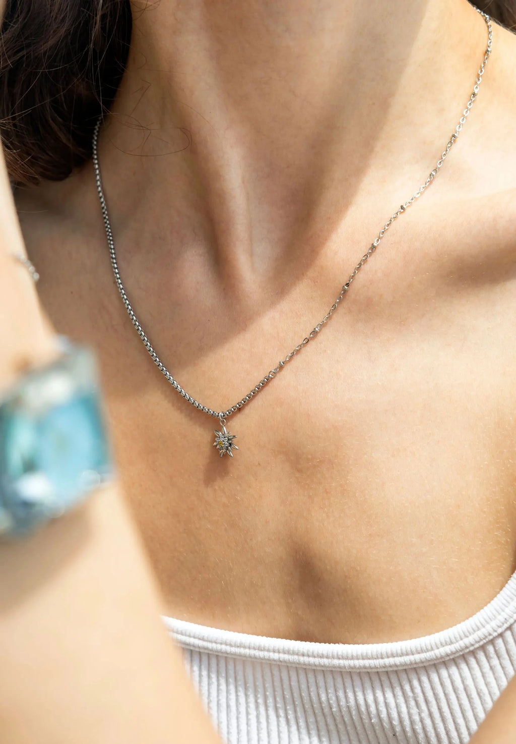 A lady wearing an Edelweiss Flower Necklace. This breathtaking pendant, adorned with 8 sparkling Cubic Zirconia stones and crafted from durable stainless steel is ads a touch of Swissness to your look.
