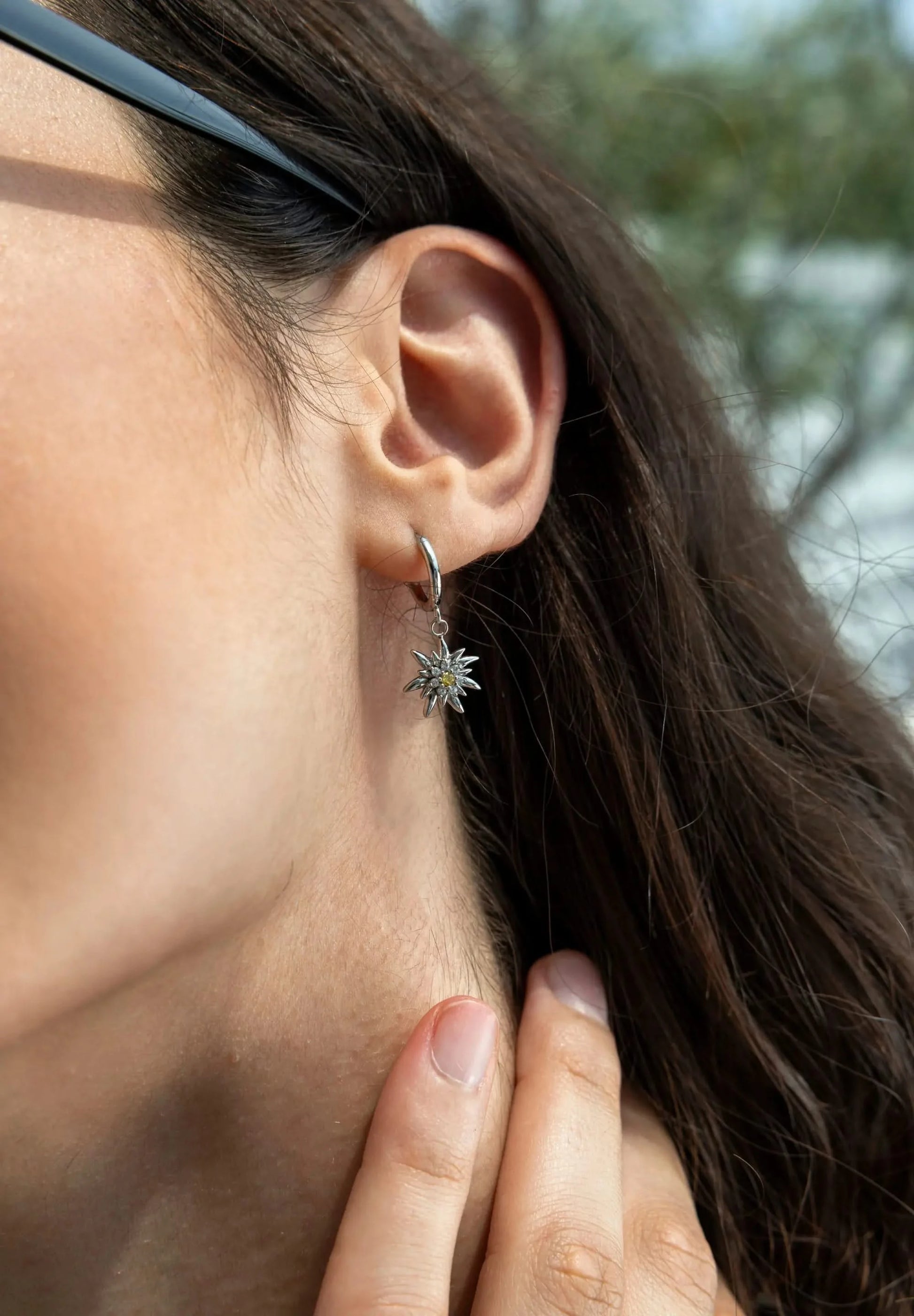 A woman is wearing a Jowissa Jewelry Earring in stainless steel, showing the Swiss flower Edelweiss. Including 8 Cubic Zirconia stones.