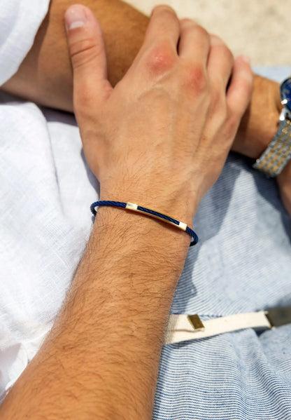 A man is wearing a stylish stainless steal bracelet in gold and blue on his wrist.