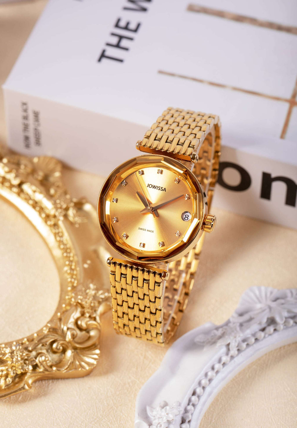 J1.282.M gold watch made for women with a luxurious gold-plated stainless steel case and bracelet. Its case features a shiny sunray dial with 11 diamond indices and Dauphine-style diamond hands, adding a touch of sparkle.
Offers a 40-hour power reserve and includes a date window. The watch is placed on a table along with a book