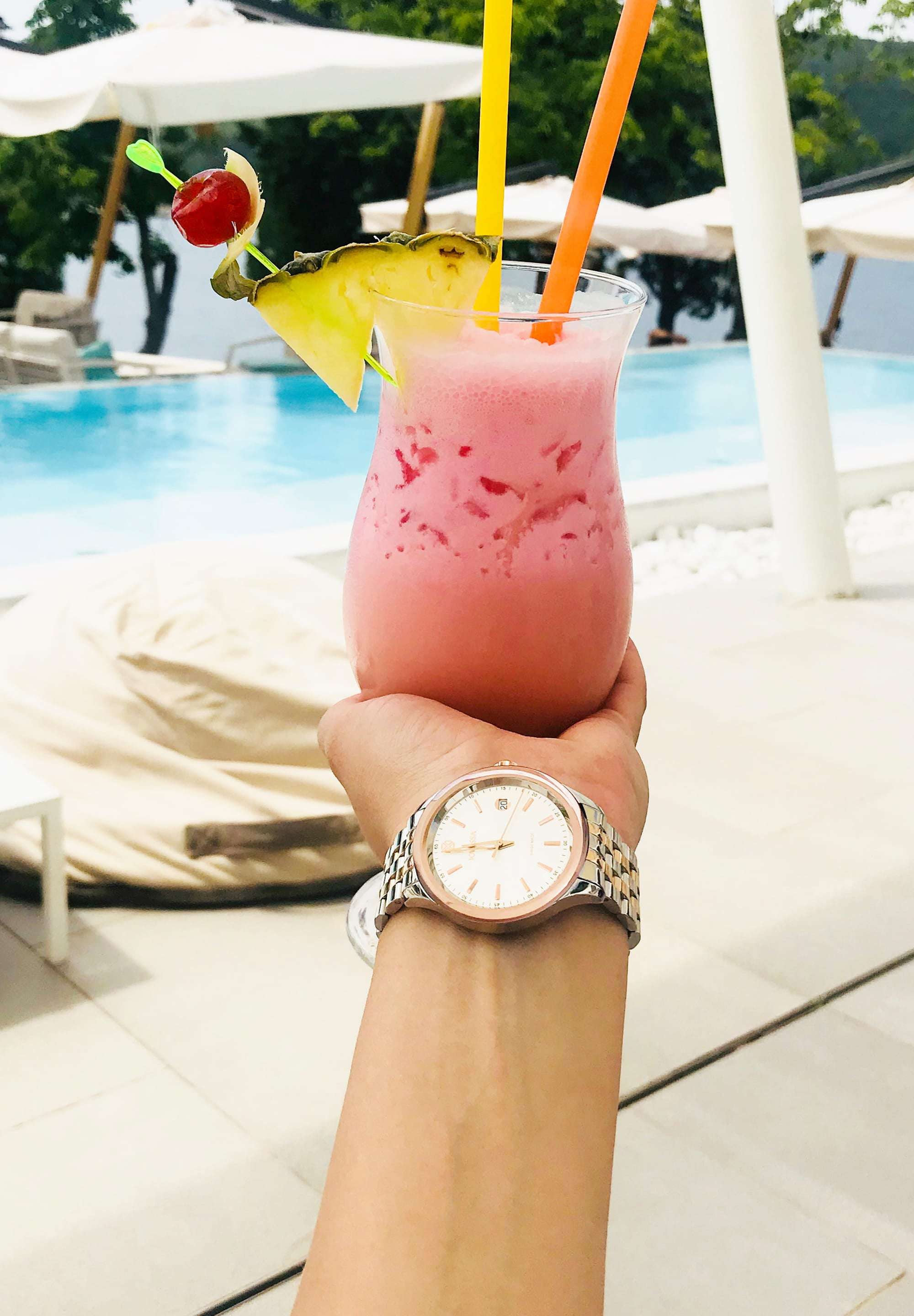 J4.229.M  medium size watch - worn by a woman with a glass of pina colada on her hand – features a stainless steel case – boasts a shiny silver dial with rose-gold hour markers – includes a calendar window - all made in switzerland