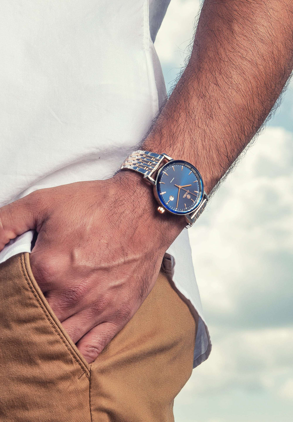 Silver swiss watch for men - all swiss made watch - silver watch with blue dial - worn by a man with white shirt and brown pants 