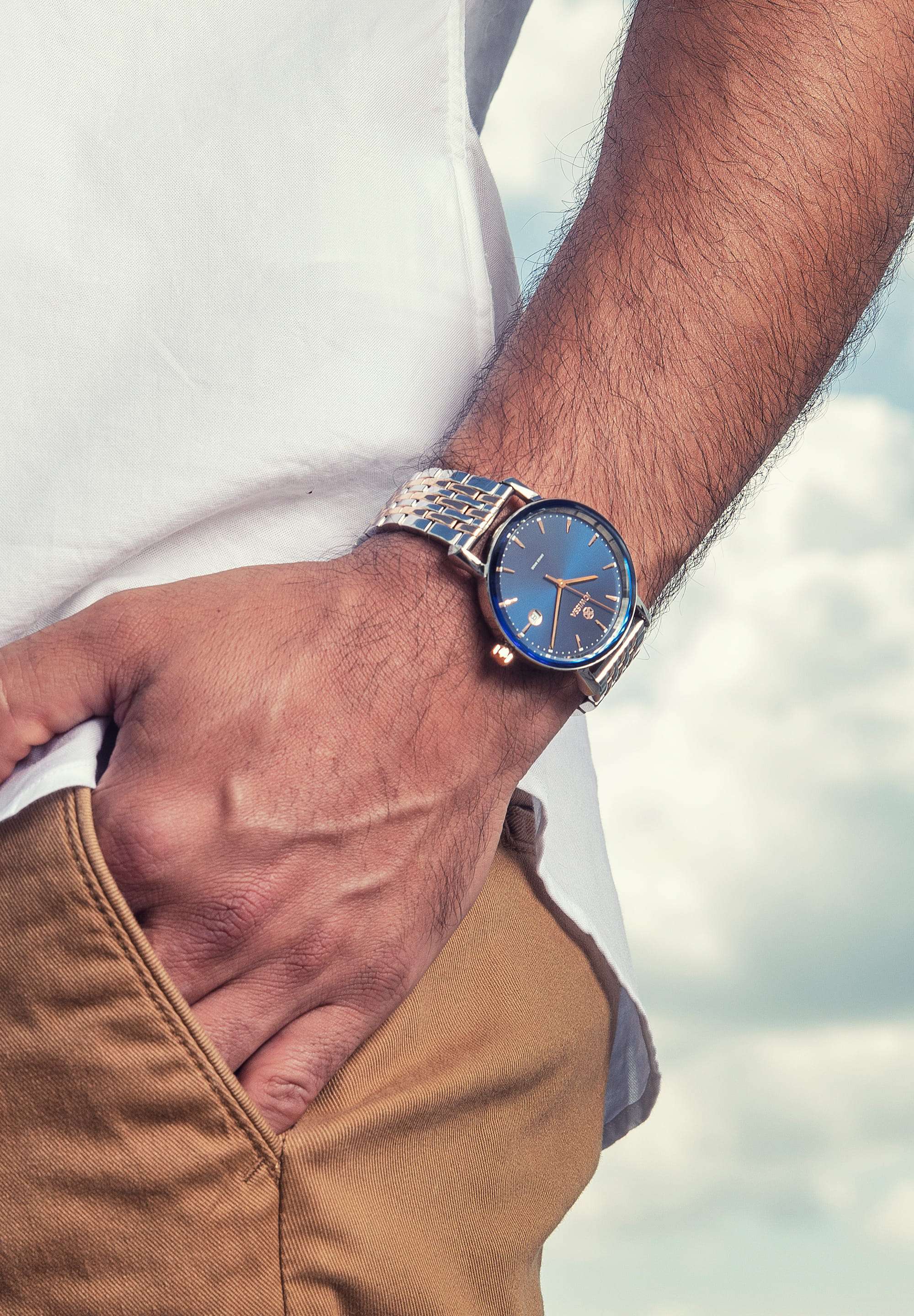 Silver swiss watch for men - all swiss made watch - silver watch with blue dial - worn by a man with white shirt and brown pants 