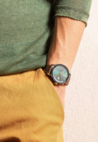 J4.557.L Virtuo Swiss watch for men - stainless steel - worn by a man with yellow pants and green shirt - with brown alligator-embossed leather strap - transparent back showcases the Swiss-made Ronda R150 automatic movement