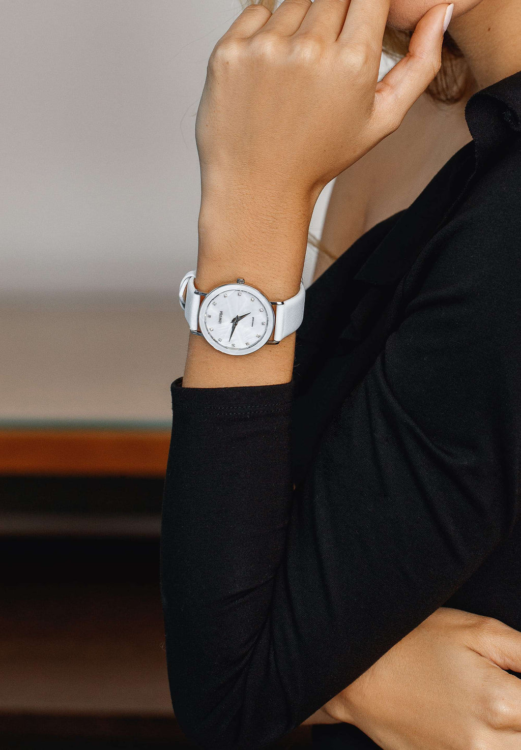 White facet watch worn by a girl with black shirt - the swiss watch has a white leather strap and silver details in the front - all swiss made watch for women