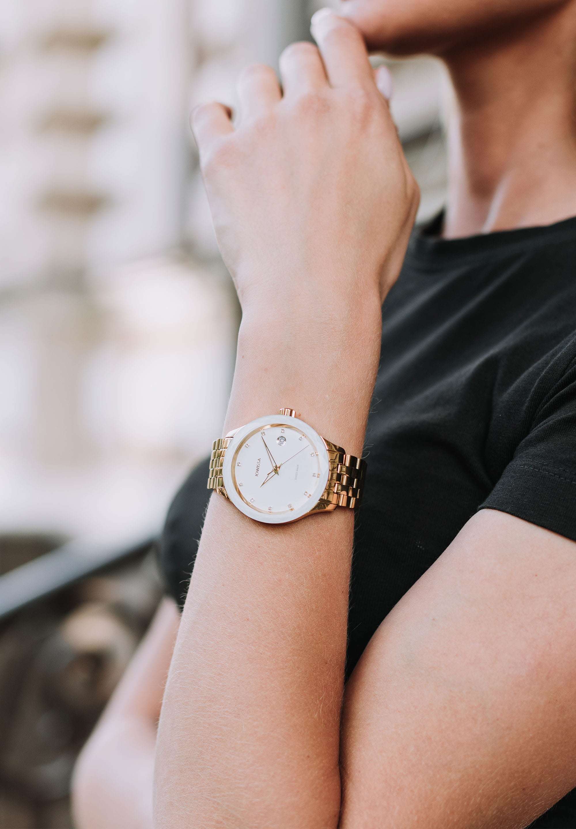 J6.237.M Swiss Made Watch worn by a woman with black shirt – has a polished gold-plated stainless steel case paired with a white sunray dial. The dial is marked with 12 rhinestone hour markers - Powered by a Ronda Swiss quartz movement, it includes a date window for added functionality.