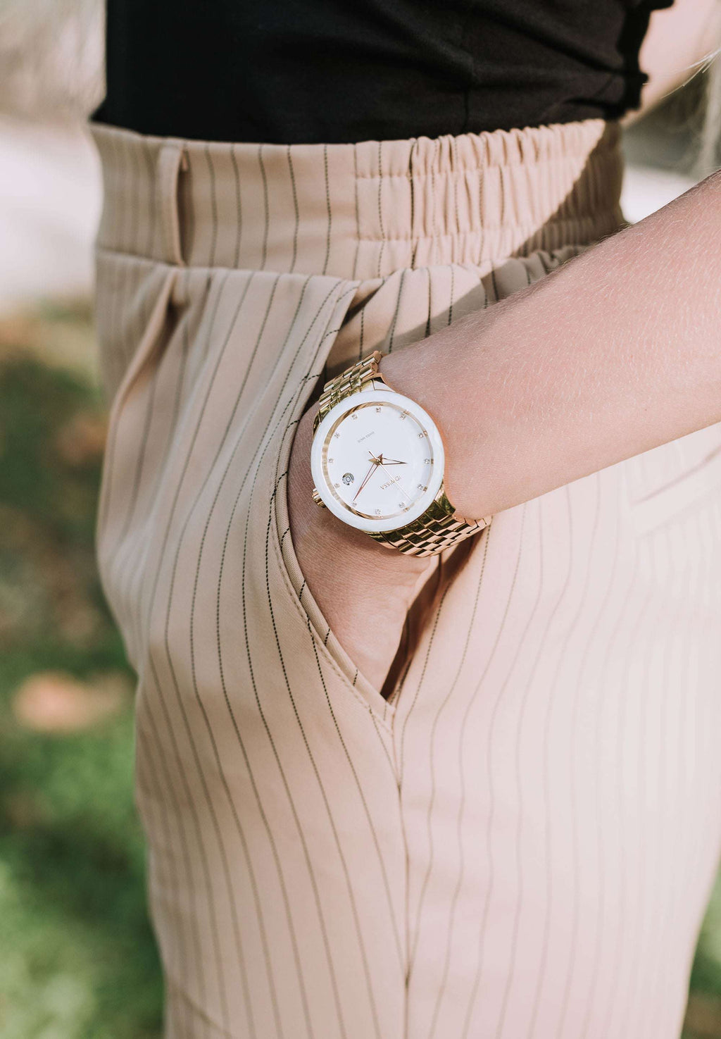 Swiss Made Watch worn by a girl who is standing – This women’s watch has a sleek gold-plated stainless steel case and a radiant white sunray dial, accented with 12 sparkling rhinestones as hour markers -with 5 ATM water resistance
