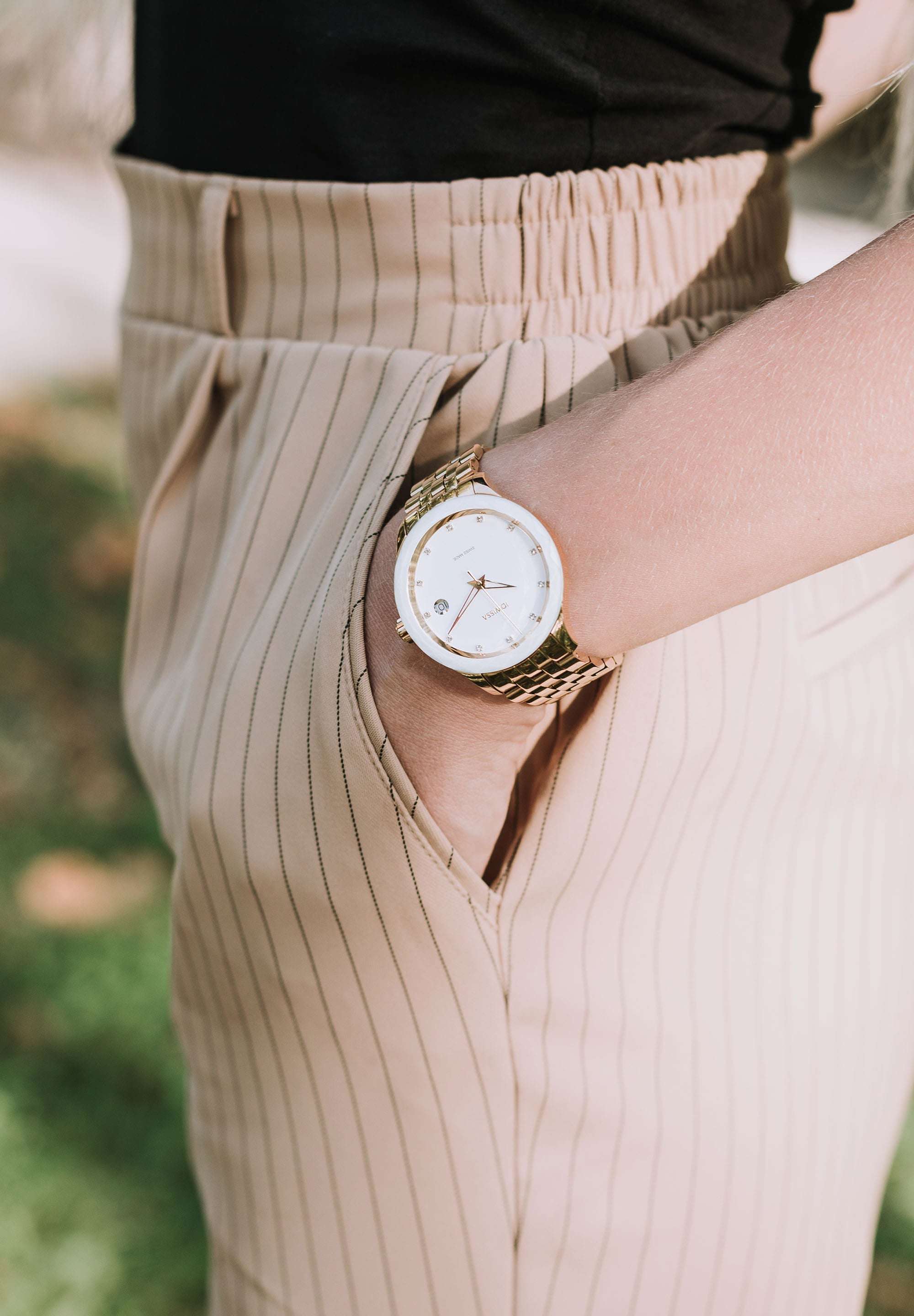 Swiss Made Watch worn by a girl who is standing – This women’s watch has a sleek gold-plated stainless steel case and a radiant white sunray dial, accented with 12 sparkling rhinestones as hour markers -with 5 ATM water resistance